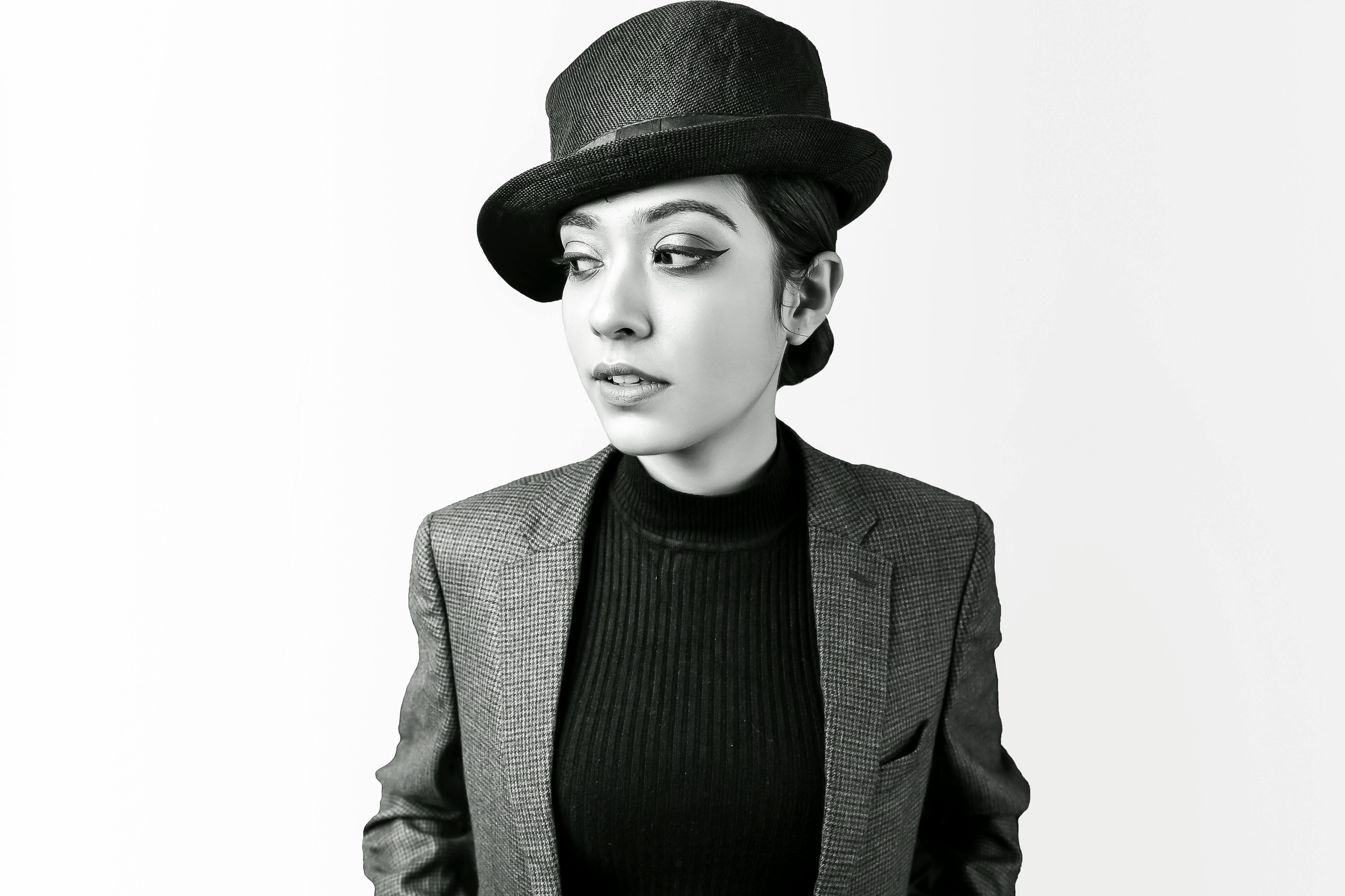 Grayscale portrait of a stylish woman in a blazer and fedora, exuding elegance.