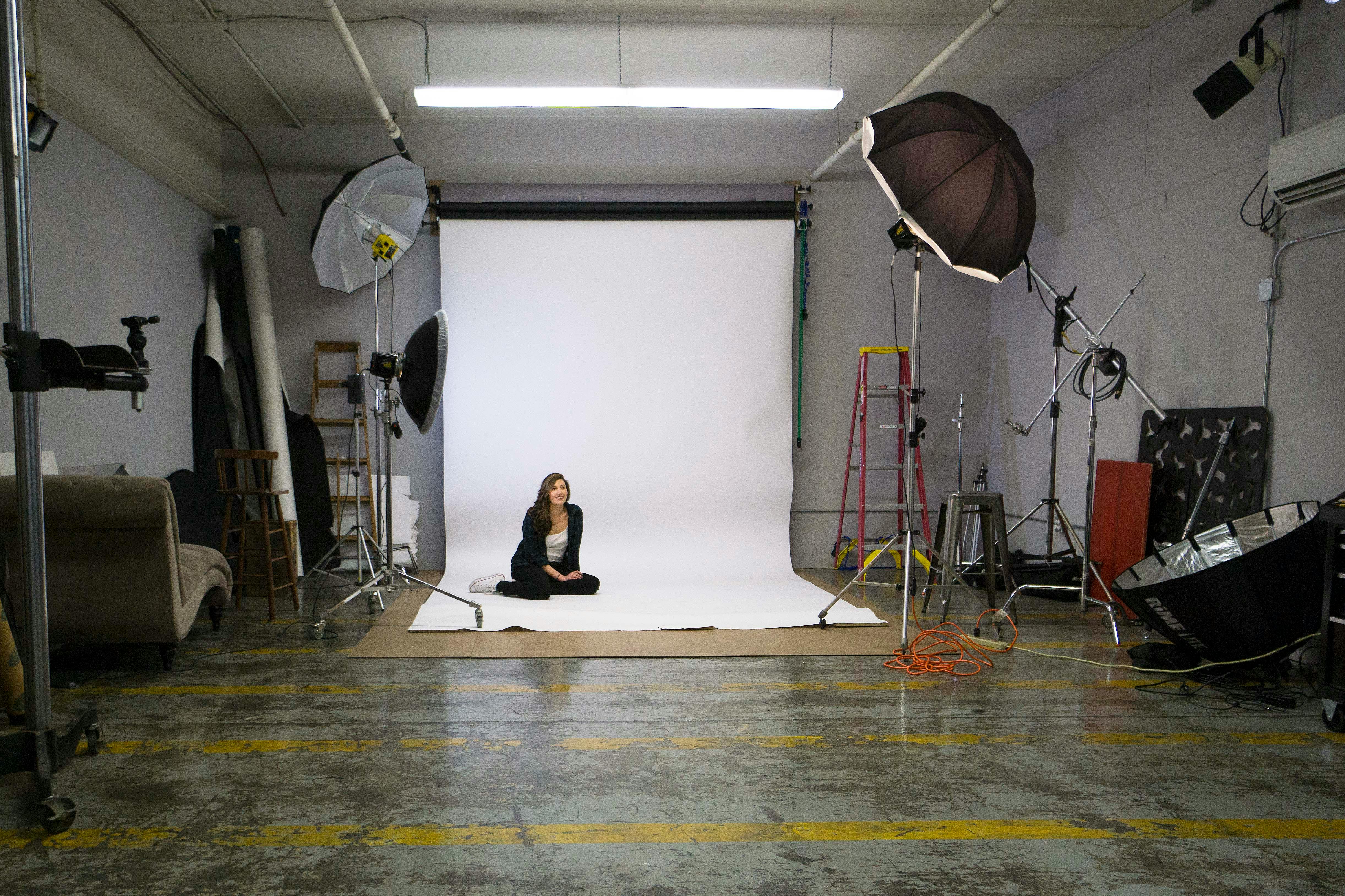 Photography studio featuring a professional setup with lighting equipment and a model sitting on the floor.