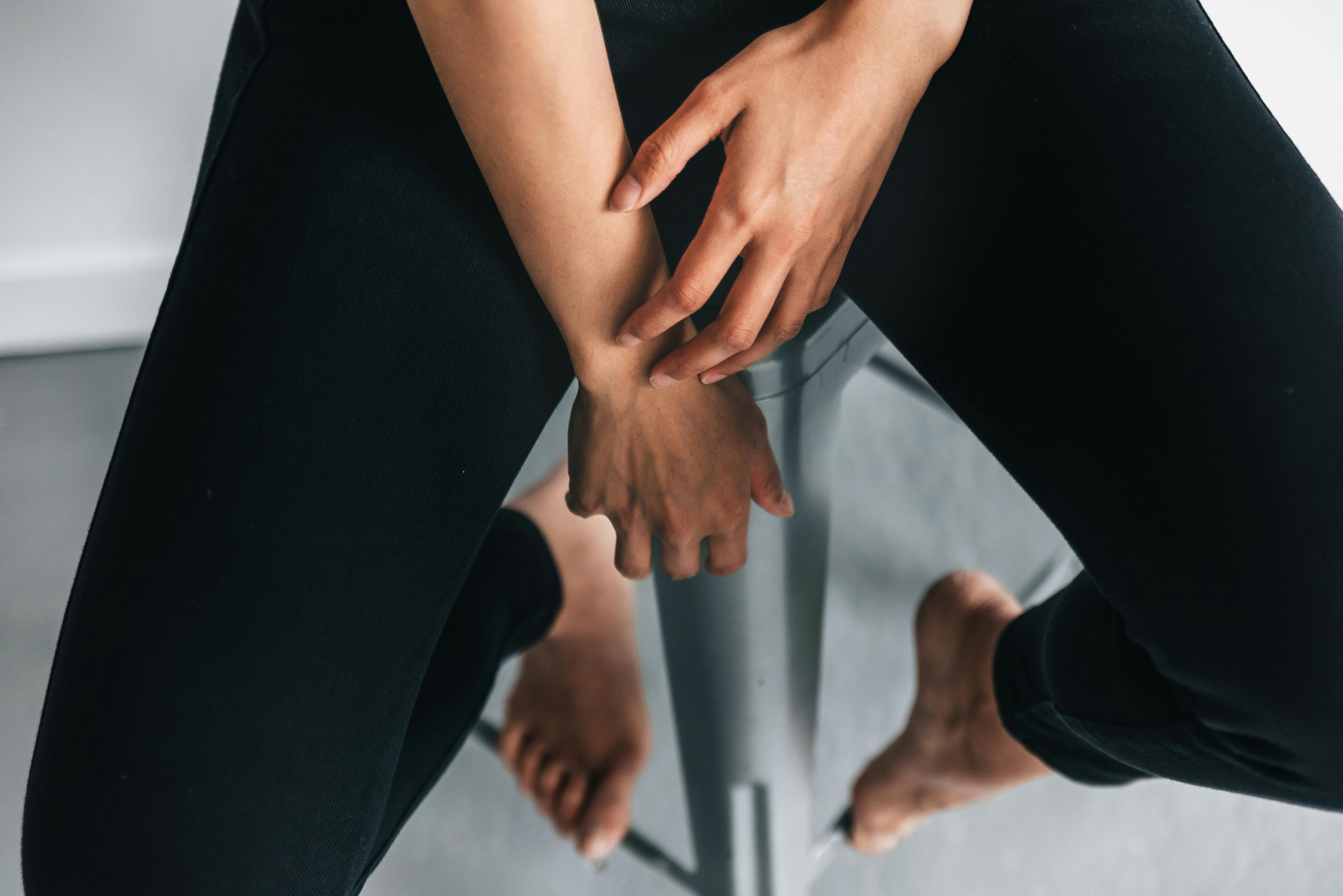 A minimalist portrait showing a barefoot person sitting on a stool indoors.